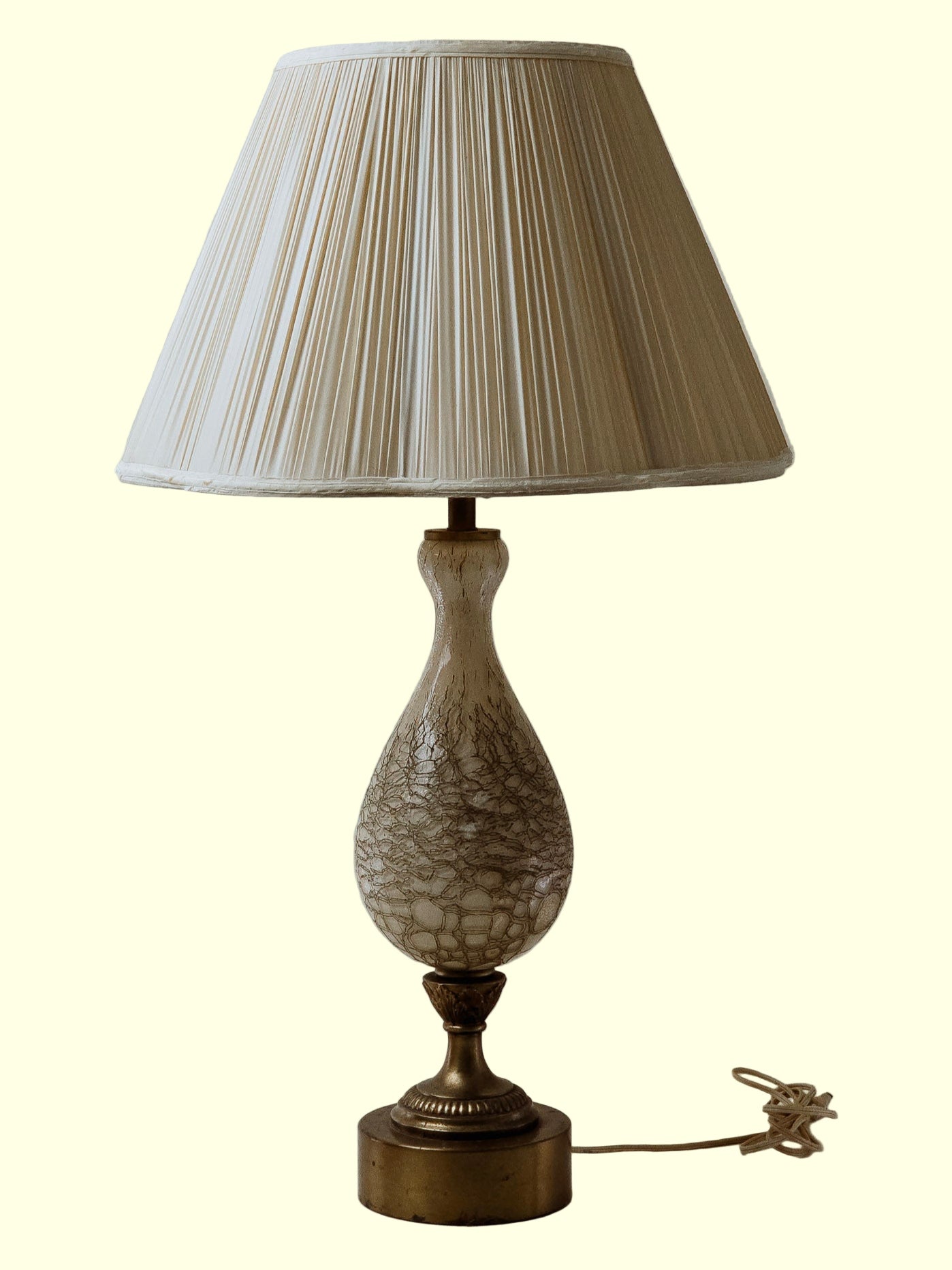 A brass and ceramic table lamp with a pleated scalloped shade, standing on a flat surface with a neutral background.