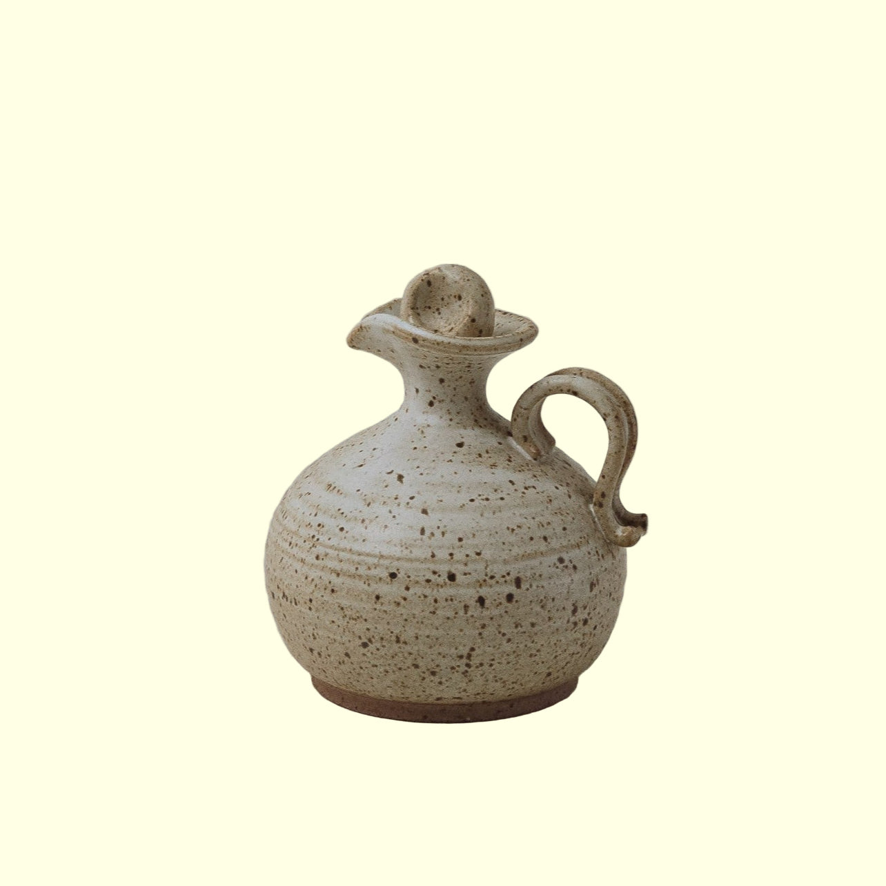 A beige ceramic dressing decanter with a matching lid, featuring a smooth, rounded body adorned with delicate speckles.