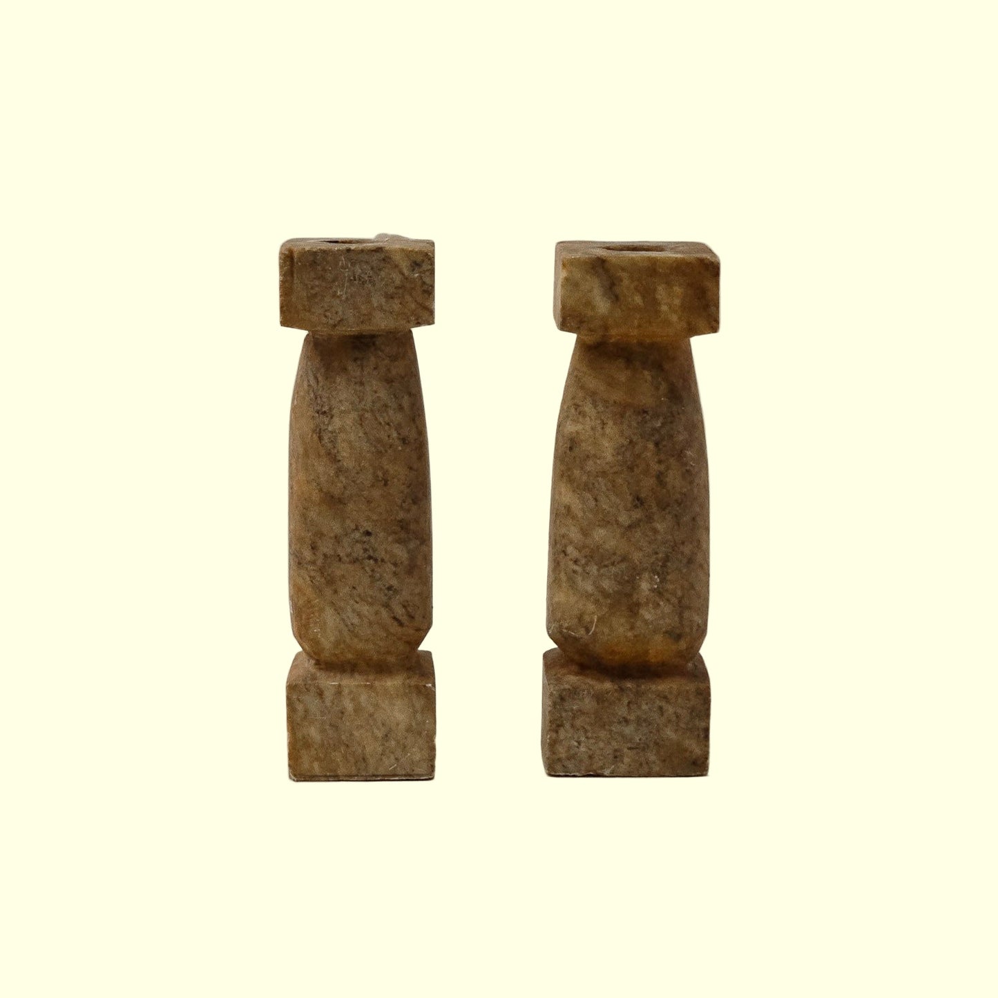 A pair of beige, textured stone candle sticks placed on a neutral background.