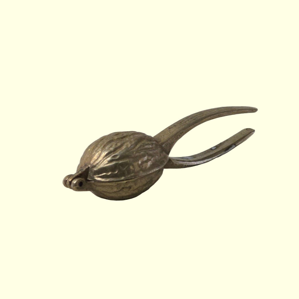 A polished brass nutcracker with a sleek design, lying on a grey surface.