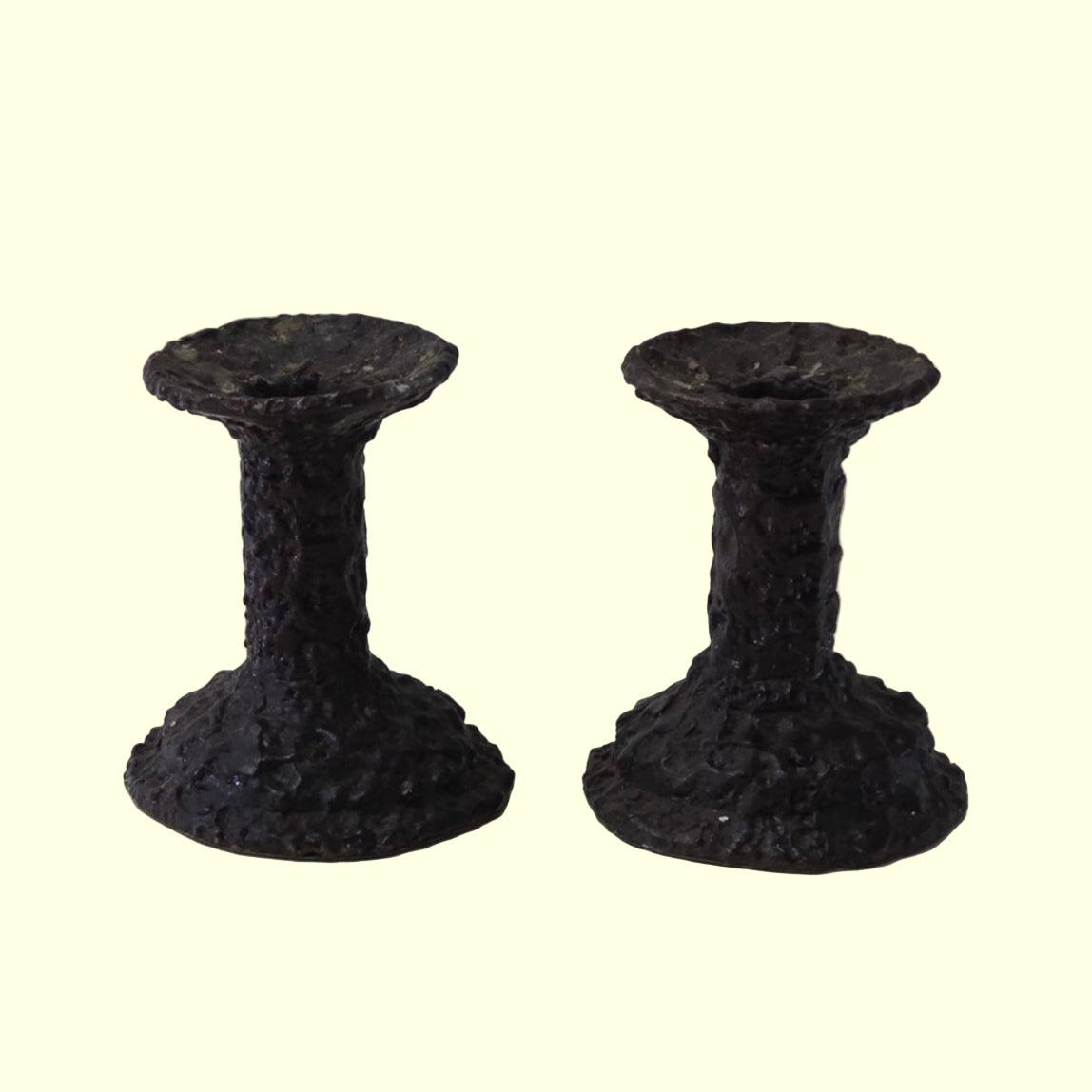A pair of dark Brutalist candle holders with a textured surface, designed for holding taper candles.
