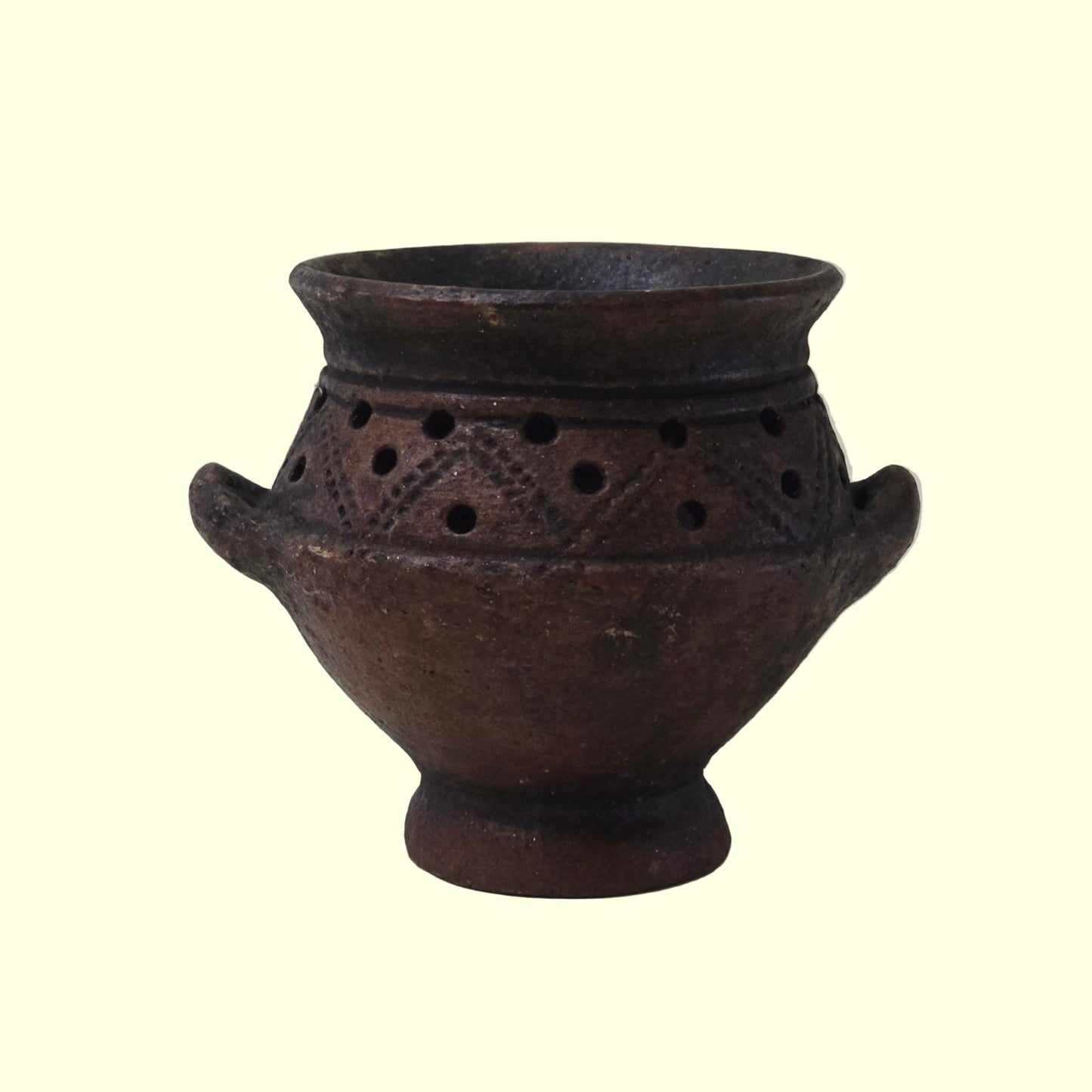 A 19th Century Primitive Clay Pot with an unglazed surface and organic shape, featuring two handles and a band of holes around the mid-section.