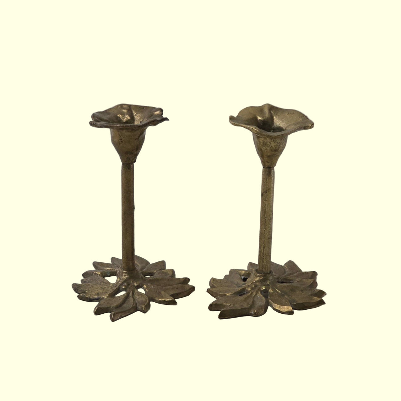 A pair of brass candle holders with floral Art Nouveau design on a grey background.