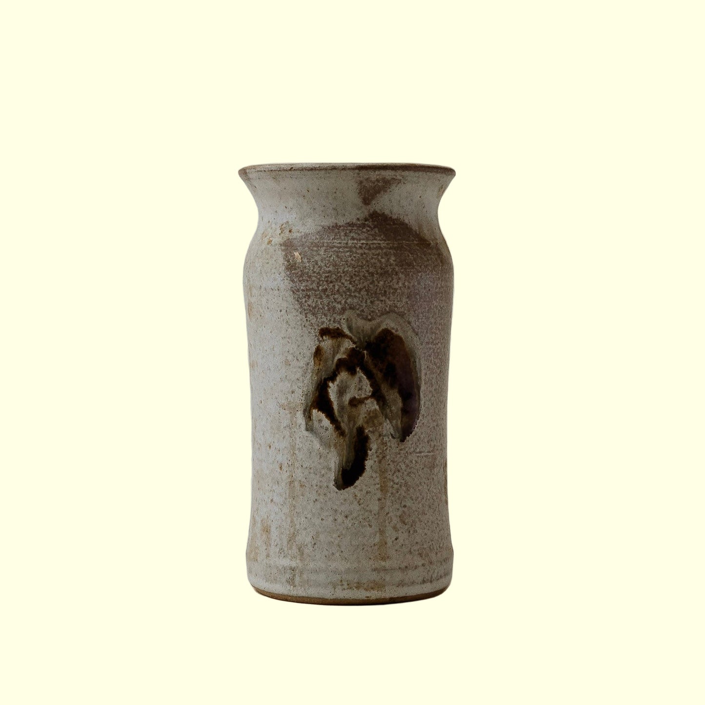 A ceramic utensil holder with a minimalist design, featuring a floral motif on the front.