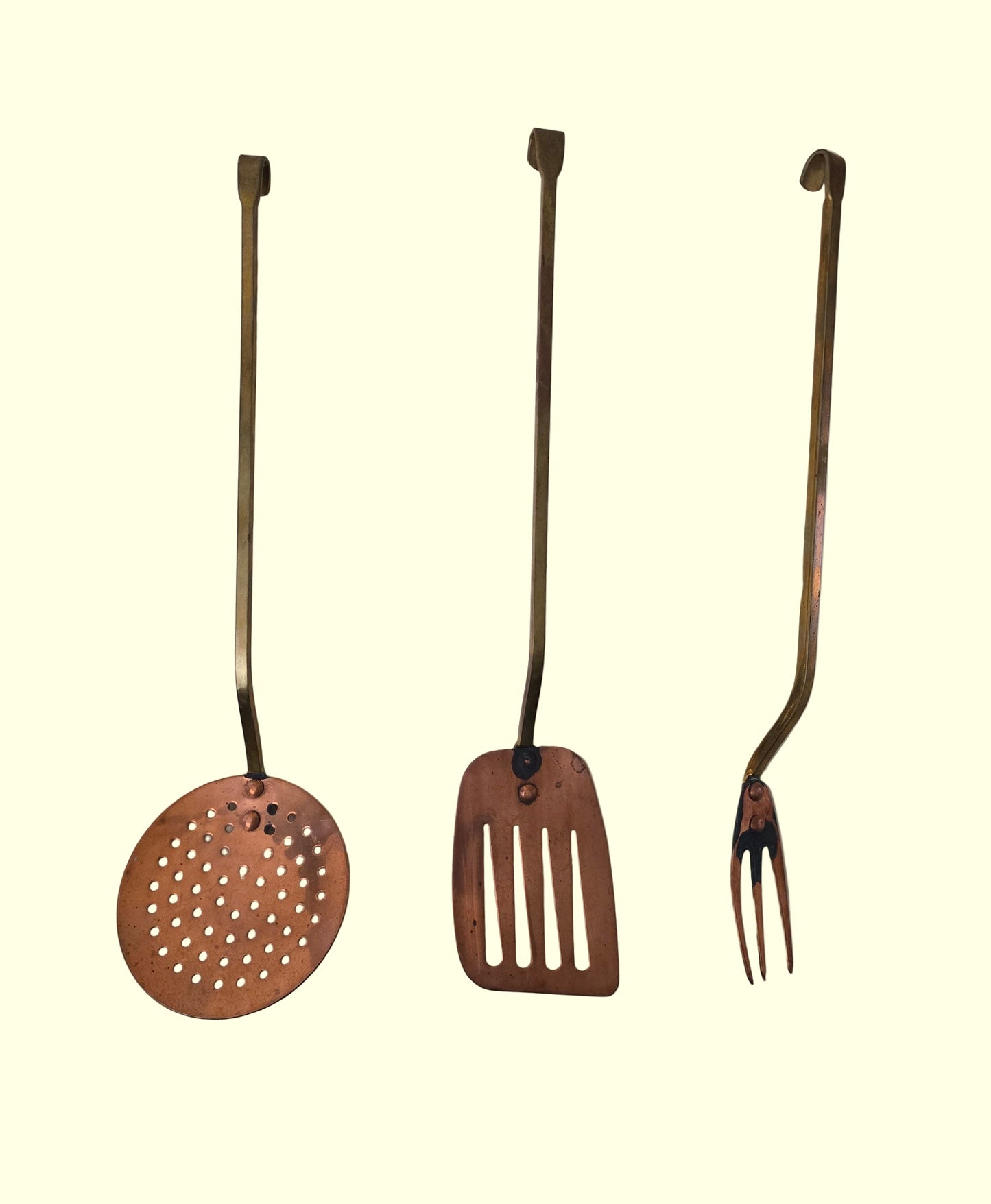 Three rustic metal kitchen utensils on a plain background