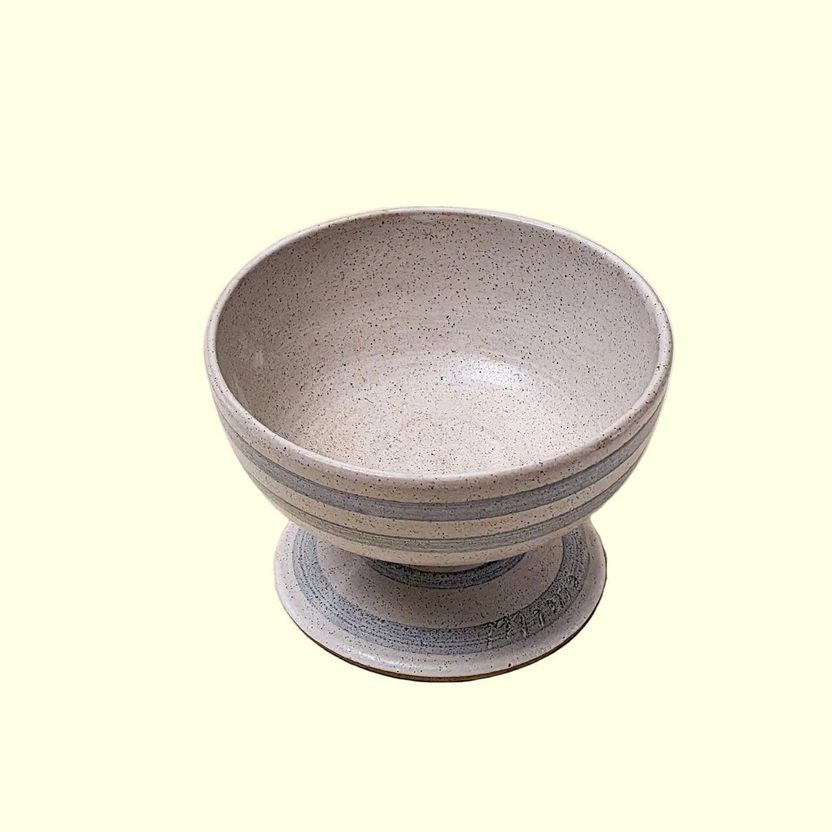 A small ceramic pedestal bowl with a speckled light gray exterior and a smooth, slightly darker gray interior, set against a plain beige background.