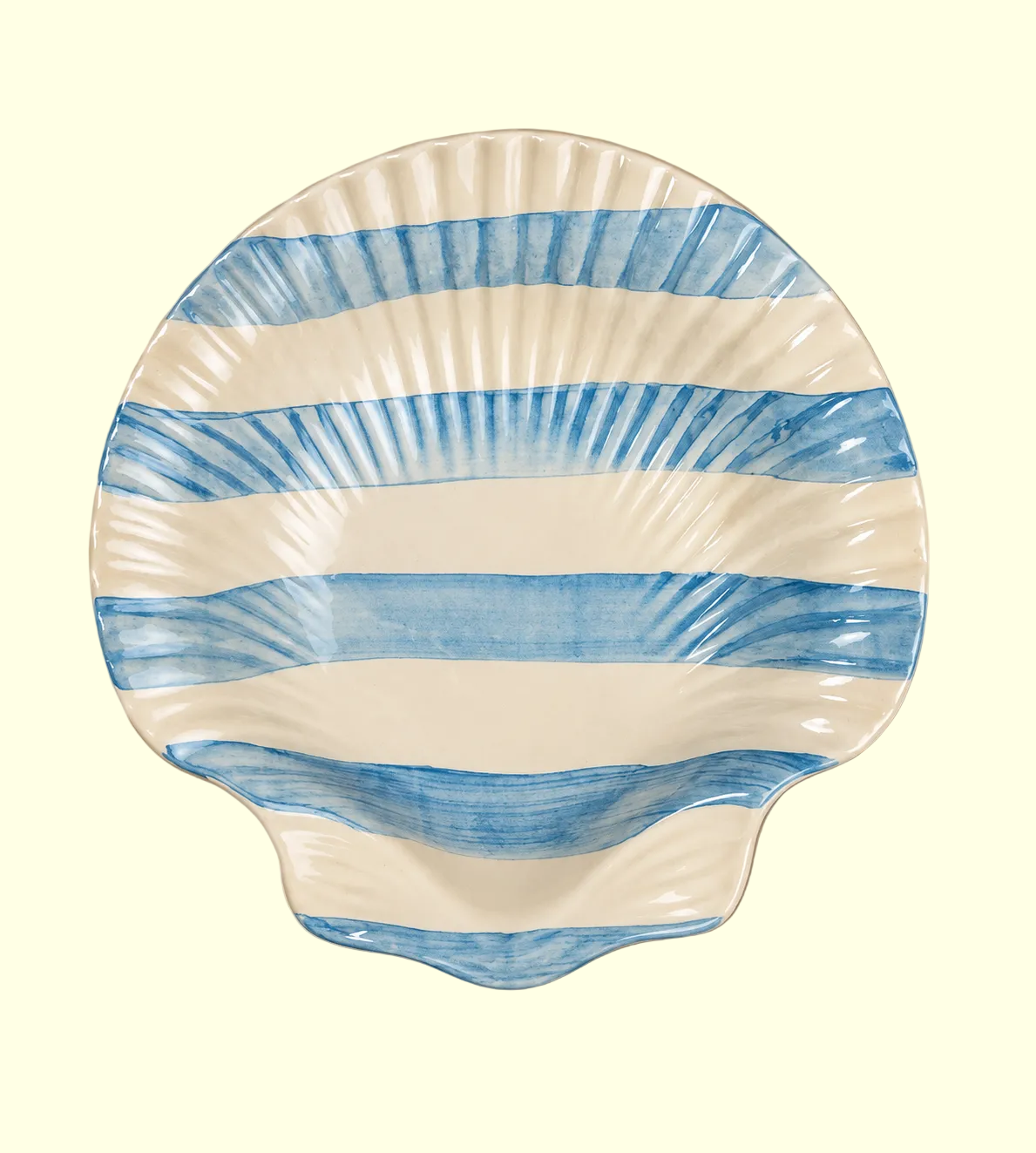 A scallop-shaped ceramic plate with blue watercolor-style horizontal stripes on an off-white background, set against a solid beige backdrop.