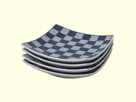 A stack of four square ceramic plates with a dark navy and light gray checkerboard pattern, set against a solid cream background.