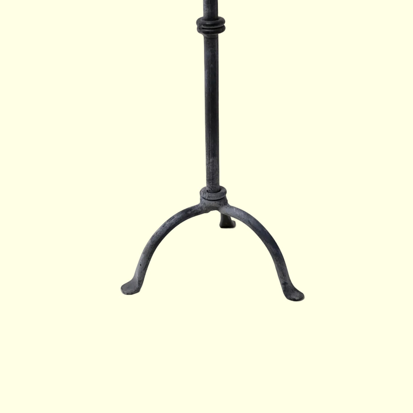 A black metal candle stick with a vertical pole and three curved legs, photographed against a plain light beige background.