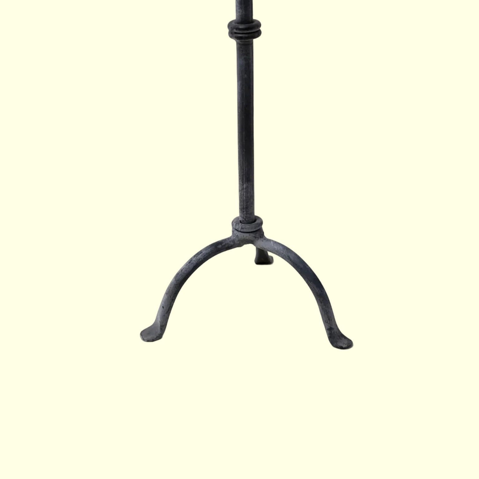 A black metal candle stick with a vertical pole and three curved legs, photographed against a plain light beige background.