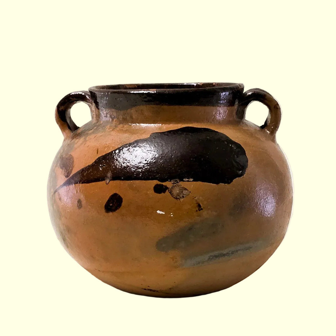 A small round ceramic pot with two loop handles, featuring a warm brown and black glaze with a glossy finish, set against a plain off-white background.