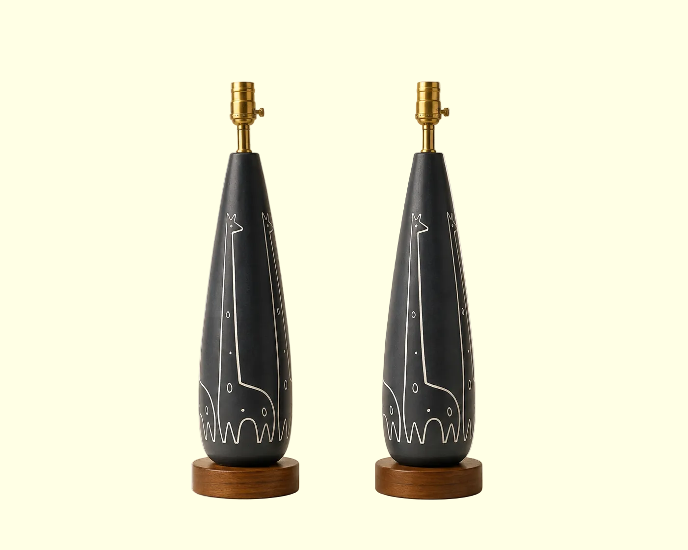 Two matching raymor table lamps with dark charcoal gray teardrop-shaped ceramic bases featuring white giraffe line drawings, mounted on round wooden bases with brass lamp sockets, set against a warm beige background.