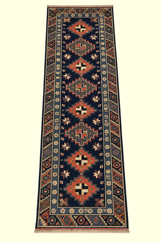 A long rectangular runner rug with a dark navy blue center field, featuring repeating diamond medallions and geometric motifs in red, beige, cream, and black, bordered by ornate floral and geometric patterns.