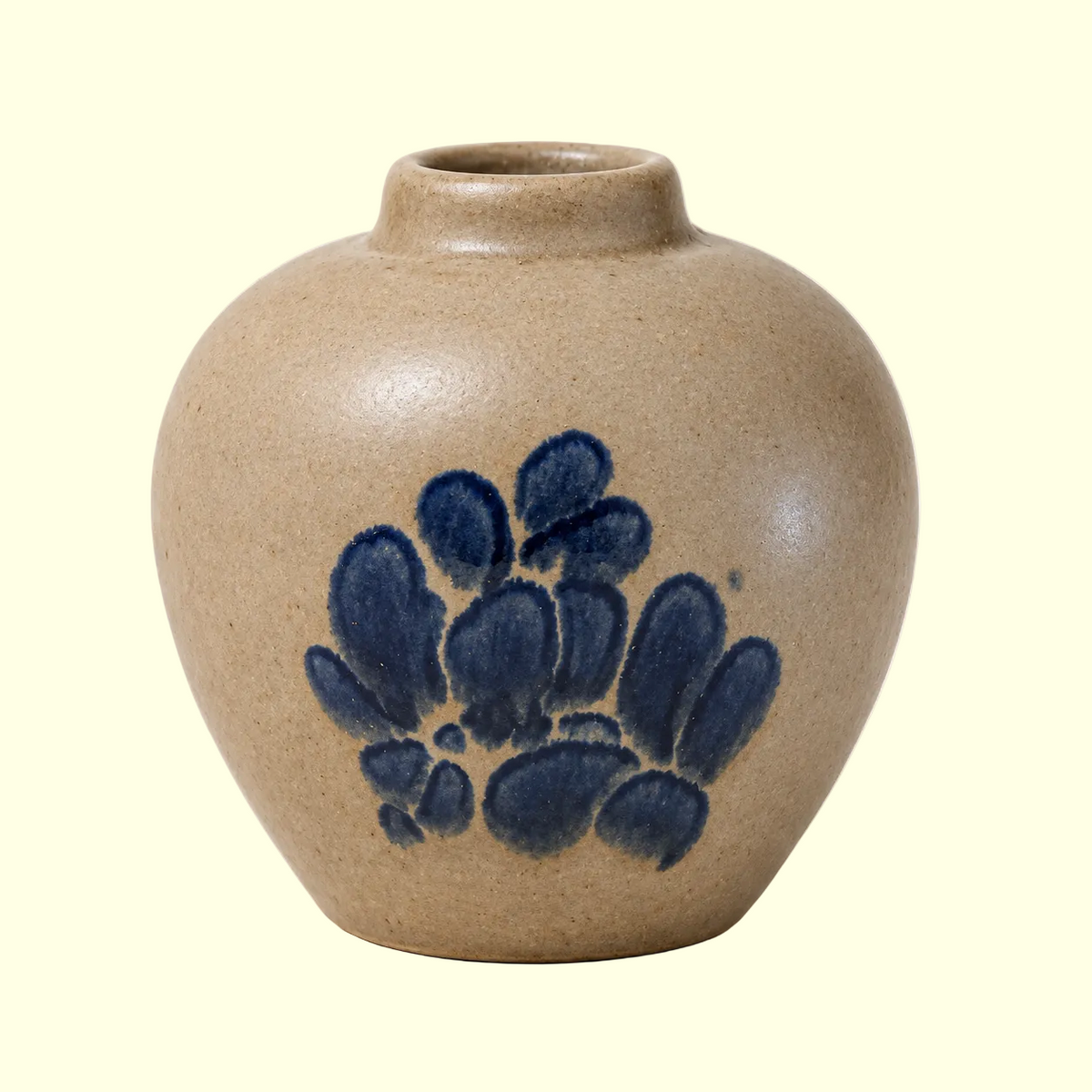 A small round ceramic vase with a short neck, featuring a speckled beige glaze and a dark blue painted floral motif on the front, set against a plain off-white background.